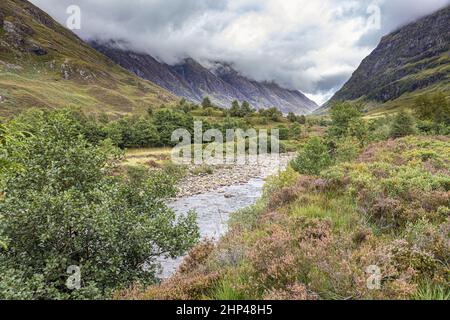 Brütende Wolken hängen über dem Fluss Coe im Tal von Glencoe, dem Ort des Massakers von 1692, Highland, Schottland, Großbritannien Stockfoto