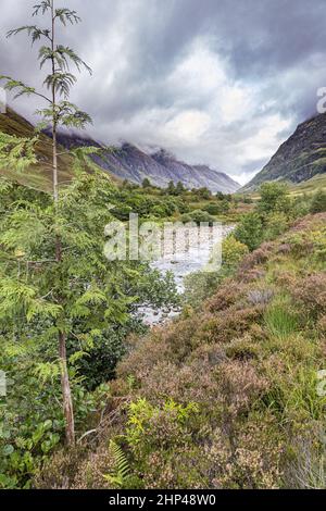 Brütende Wolken hängen über dem Fluss Coe im Tal von Glencoe, dem Ort des Massakers von 1692, Highland, Schottland, Großbritannien Stockfoto