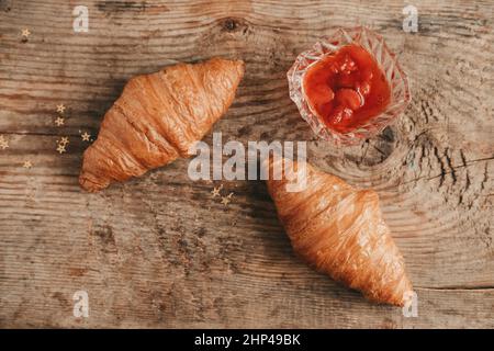 Zwei Croissants mit Erdbeermarmelade auf einem Holzhintergrund, Draufsicht. Süßes und herzhaftes Frühstück mit Croissants Stockfoto