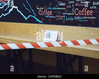 Russland, Sotschi 02.11.2021. Ein Schild mit der Aufschrift covid-19 free Zone steht auf einer hölzernen Theke des Cafés mit einem Sperrband im Vordergrund. Sel Stockfoto