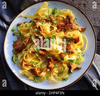 Tagliatelle Pasta mit gebratenen in Butter Pfifferlinge Pilze mit Knoblauch und fein gehackte Petersilie auf karierte Serviette auf einem rustikalen Hintergrund . Obere V Stockfoto