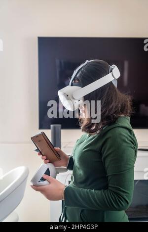 Mädchen mit VR-Headset und zwei Controllern sitzen auf ihrem Spiel, London, Großbritannien Stockfoto