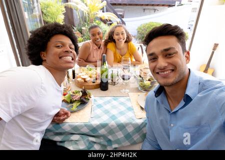 Portrait von jungen birazialen Männern mit weiblichen Freunden, die gemeinsam am Tisch essen Stockfoto