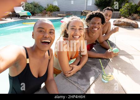 Fröhliche, multirassische Frau, die an sonnigen Tagen Selfie mit Freunden am Pool schießt Stockfoto