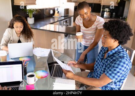 Multirassische Geschäftskollegen diskutieren über Dokumente von Geschäftsfrau mit Laptop Stockfoto