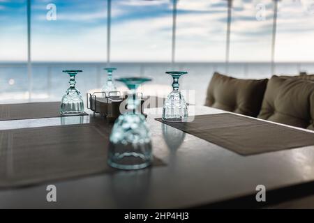 Eine Gruppe von kristallklaren Gläsern steht auf einem Tisch in einem Restaurant, vor dem Hintergrund kann man den Himmel von einem großen Panoramafenster aus sehen Stockfoto