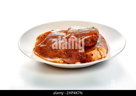 Schweinefleisch in Marinade liegt auf einem weißen Teller auf einem weißen isolierten Hintergrund. Hochwertige Fotos Stockfoto