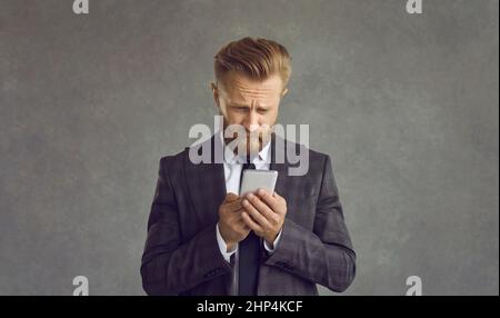 Unglücklicher Geschäftsmann isoliert auf grauem Hintergrund mit Problem mit dem Mobiltelefon Stockfoto