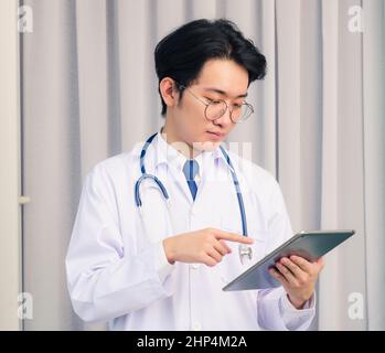 Porträt Nahaufnahme von glücklich asiatische junge Arzt schöner Mann lächelnd In Uniform und Stethoskop Halsband halten und Punkt smart Digitales Tablet und Toilette Stockfoto