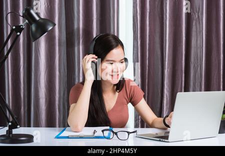 Arbeiten von zu Hause, asiatische junge Geschäftsfrau Lächeln tragen Kopfhörer Video-Telefonkonferenz oder facetime von Laptop-Computer-Meeting mit Team am Schreibtisch am h Stockfoto