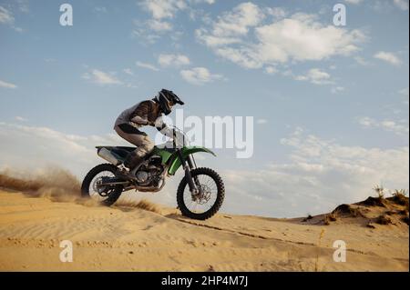 Professioneller Motocross-Fahrer auf Helm und Schutzanzug, der über Sandhügel gleitet. Speedmoto-Rennen in der Wüste Stockfoto