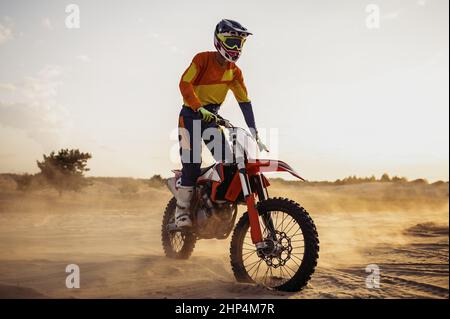 Motocross-Fahrer trägt Schutzhelm und Anzug auf Sport-Motorrad in der Wüste Stockfoto