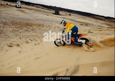 Professioneller Motocross-Fahrer auf Helm und Schutzanzug, der den Sandberg hinunterrutscht. Speed Moto Racing Stockfoto