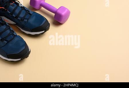 Zwei blaue Turnschuhe und lila Hanteln auf beigem Hintergrund, Sport. Speicherplatz kopieren Stockfoto