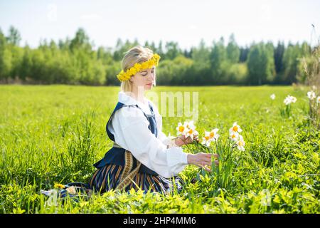 Junge Frau in Nationalkleid auf einem Feld mit Narzissen Blumen. Stockfoto