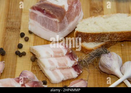 Traditionelles ukrainisches Lebensmittelkonzept mit Weißbrot. Ukrainischer roher Schmalz mit Pfefferkorn und Knoblauch, Messer, salo-Scheiben, die auf Holzschneidschweinen liegen Stockfoto