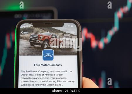 Die Aktienkursentwicklung der Ford Motor Company mit Grafiken im Hintergrund. Man hands Holding a Smartphone with Logo on the screen, February 2022, San Francisco, USA. Stockfoto