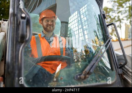Lächelnder Bauarbeiter, der das Fahrzeug im Taxi fährt. Nahaufnahme des Schwerlastbedieners Stockfoto