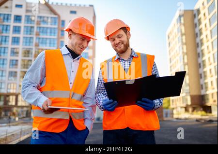 Lächelnde Bauarbeiter diskutieren über den Grundriß. Hauptingenieur, der der Fachfirma Bericht erstattet Stockfoto