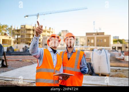 Mitarbeiter, der dem Auftragnehmer über die Ausführung des Bauplans mit Tablet auf der Baustelle berichtet Stockfoto