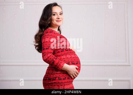 Eine schöne junge Brünette mit langen Haaren in einem roten Kleid auf weißem Hintergrund schaut in die Kamera, ein Ort für Text Stockfoto