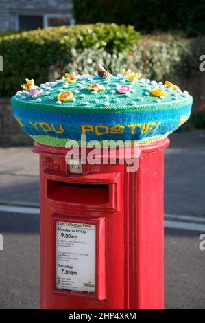 Vielen Dank. Farbenfrohe, handgestrickte Wollmütze ziert eine traditionelle rote Säulenbox in Anerkennung der wesentlichen Arbeit des lokalen Postboten. Stockfoto