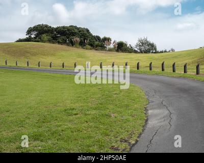 Kurvige Asphaltstraße mit Holzpfosten auf grünem Hügel Stockfoto