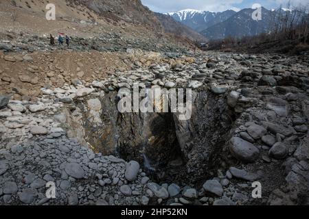 (220218) -- SRINAGAR, 18. Februar 2022 (Xinhua) -- Menschen gehen in der Nähe einer vertikalen Sinkhole, die sich in der Mitte eines Flussbettes in einem Dorf in Anantnag Bezirk, etwa 94 km südlich von Srinagar Stadt, der Sommerhauptstadt des von Indien kontrollierten Kaschmir, entwickelt hat, 18. Februar 2022. Eine vertikale Sinkhole, die sich in der Mitte eines Flussbettes entwickelt hat, hat einen Süßwasserstrom im von Indien kontrollierten Kaschmir verschlungen, sagten Beamte am Donnerstag. Das Sinkhole wurde in allen Lauf des Bachwassers in sie entwässert und ließ den stromabwärts gelegenen Teil trocken und tötete Forellenfische in großer Zahl. Es hat auch zu immasu geführt Stockfoto