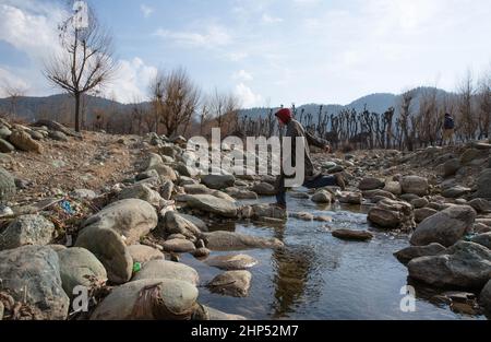 (220218) -- SRINAGAR, 18. Februar 2022 (Xinhua) -- Ein Junge durchquert einen teilweise getrockneten Bach in einem Dorf im Bezirk Anantnag, etwa 94 km südlich der Stadt Srinagar, der Sommerhauptstadt des von Indien kontrollierten Kaschmir, am 18. Februar 2022. Eine vertikale Sinkhole, die sich in der Mitte eines Flussbettes entwickelt hat, hat einen Süßwasserstrom im von Indien kontrollierten Kaschmir verschlungen, sagten Beamte am Donnerstag. Das Sinkhole wurde in allen Lauf des Bachwassers in sie entwässert und ließ den stromabwärts gelegenen Teil trocken und tötete Forellenfische in großer Zahl. Es hat auch unermessliche Schäden an der Wasserwelt verursacht. (Xinhua/Javed Da Stockfoto