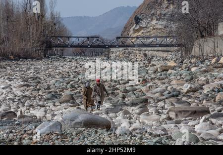 (220218) -- SRINAGAR, 18. Februar 2022 (Xinhua) -- Menschen gehen in einem trockenen Bach in einem Dorf im Anantnag-Bezirk, etwa 94 km südlich von Srinagar, der Sommerhauptstadt des von Indien kontrollierten Kaschmir, am 18. Februar 2022. Eine vertikale Sinkhole, die sich in der Mitte eines Flussbettes entwickelt hat, hat einen Süßwasserstrom im von Indien kontrollierten Kaschmir verschlungen, sagten Beamte am Donnerstag. Das Sinkhole wurde in allen Lauf des Bachwassers in sie entwässert und ließ den stromabwärts gelegenen Teil trocken und tötete Forellenfische in großer Zahl. Es hat auch unermessliche Schäden an der Wasserwelt verursacht. (Xinhua/Javed Dar) Stockfoto