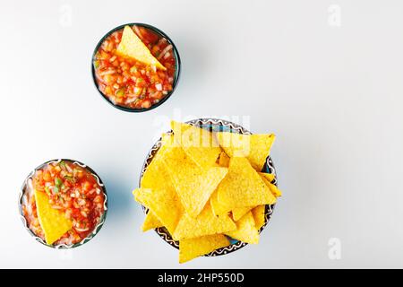 Zwei Schüsseln mit Salsa-Sauce und Nacho-Chips auf weißem Hintergrund. Tortilla-Chips und Salsa tauchen in eine Schüssel. Konzept der mexikanischen Küche. Draufsicht. Speicherplatz kopieren Stockfoto