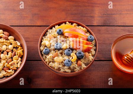 Leckere Haferflocken mit Beeren, Nüssen und Äpfeln auf einem Holztisch. Schüssel Haferbrei mit Heidelbeeren und Honig. Gesundes Frühstück. Draufsicht Stockfoto