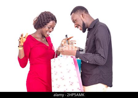 Glücklicher junger Mann, der seiner Freundin Geschenke in einer Einkaufstasche zeigt. Stockfoto