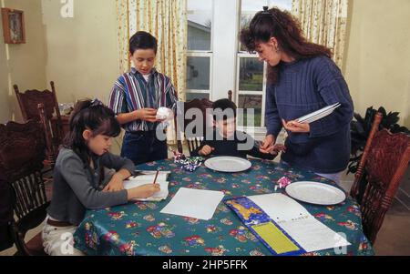 Austin Texas USA, 1995: Die alleinerziehende hispanische Mutter mit drei Kindern stellt den Tisch für das Abendessen, während die Tochter Hausaufgaben macht. HERR EC-031 ©Bob Daemmrich Stockfoto