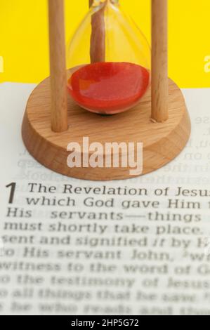 Rote Sanduhr auf der Oberseite der Bibel, geöffnet in der Offenbarung Jesu Christi Kapitel 1. Stockfoto