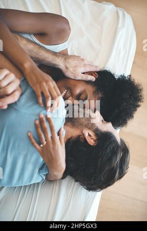 Ich kann nicht anders, als dich zu küssen, wann immer ich kann. Hochwinkelige Aufnahme eines anhänglichen Mannes mittleren Alters, der seine Frau auf ihre Stirn küsst, während er auf ihrem Bett liegt Stockfoto
