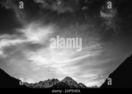 Wolken bei Sonnenuntergang auf einem verschneiten Berg in Italien, schwarz-weiß. Monochrom Stockfoto