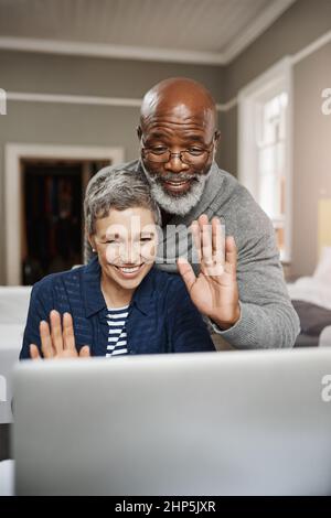 Verbinden Sie sich mit Ihren Lieben, wo immer Sie sind. Aufnahme eines älteren Paares, das während der Verwendung eines Laptops zu Hause winkt. Stockfoto