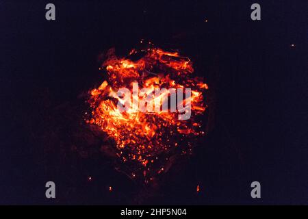 Der Blick auf ein sterbendes Lagerfeuer, bereit zum Schnappen mit glühender Glut, die mit oranger Flamme auf schwarzem Hintergrund brennt. Stockfoto