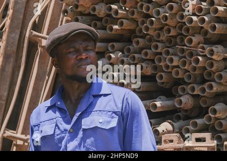 Selektiver Fokus auf den schwarzen afrikanischen Arbeiter in blauer Uniform, der für das Altmetalllager für das Recycling arbeitet. Abu Dhabi, VAE Stockfoto