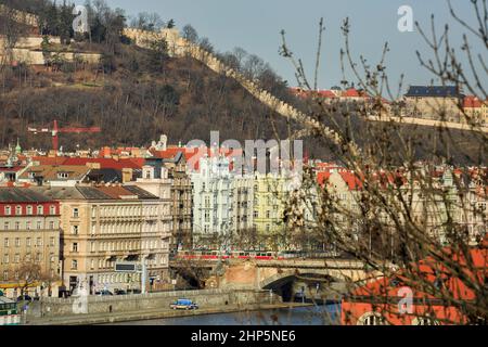 Kastellationen der Burgmauer auf dem Petrin-Hügel, Hradcany, Prag, Tschechische republik, von der Vysehrad-Festung aus gesehen, mit der Moldau und einem roten Zug unten Stockfoto