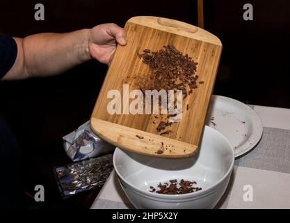 Eine Frauenhand gießt Stücke Zimtstangen in einen Behälter für eine Teemischung. Zimtstangen auf einem Holzbrett. Gesunde Lebensmittel CO Stockfoto