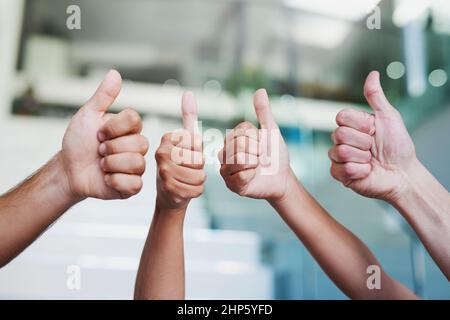 100 genehmigt. Zugeschnittene Aufnahme einer Gruppe von Händen, die in einem Büro Daumen nach oben zeigen. Stockfoto