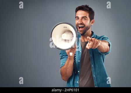 Du bist unser Gewinner des Tages. Studioaufnahme eines hübschen jungen Mannes mit einem Megaphon vor grauem Hintergrund. Stockfoto