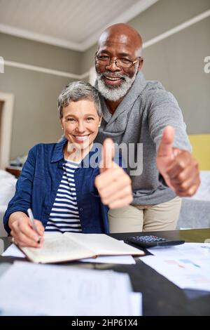 Unsere Finanzen sind in Ordnung. Ein beschnittenes Porträt eines älteren Ehepaars, das Ihnen den Daumen nach oben gibt, während Sie zu Hause an ihren Finanzen arbeiten. Stockfoto