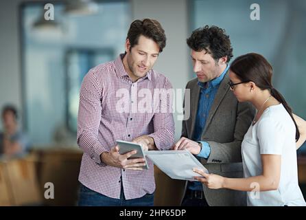 Ideen in die Realität umsetzen. Aufnahme einer Gruppe von Kollegen, die in einem Büro stehen und über ein digitales Tablet reden. Stockfoto