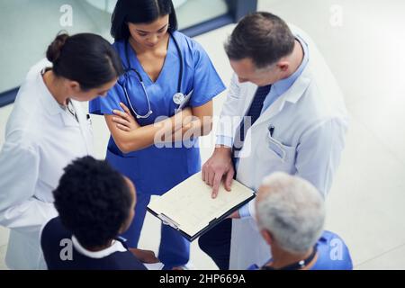 Gibt die Dosierung für diesen Patienten an. Aufnahme einer Gruppe von Ärzten, die sich über eine Krankenakte unterhalten, während sie in einem Krankenhaus stehen. Stockfoto