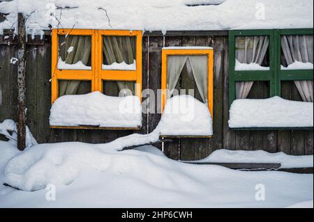 Schneebedeckte bunte Fensterrahmen durch einen Holzzaun, Dekorationen auf dem Kinderspielplatz Stockfoto