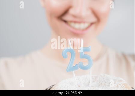 Die glückliche Frau macht einen Wunsch und bläst die Kerzen auf dem Kuchen zum 25. Geburtstag aus. Mädchen feiert Geburtstag. Stockfoto