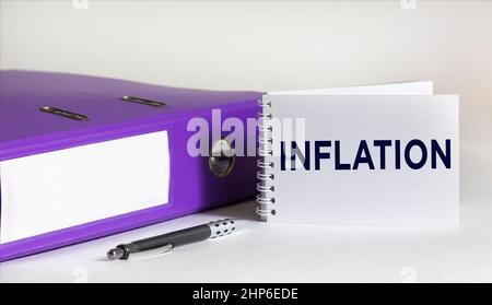 Das Wort Inflation wird auf einem Notizblock und einem weißen Hintergrund mit einem Stift und einem Ordner für Dokumente geschrieben. Stockfoto